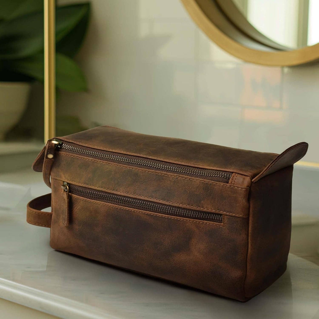 Brown leather toiletry bag with top zip, front pocket, and adjustable crossbody strap