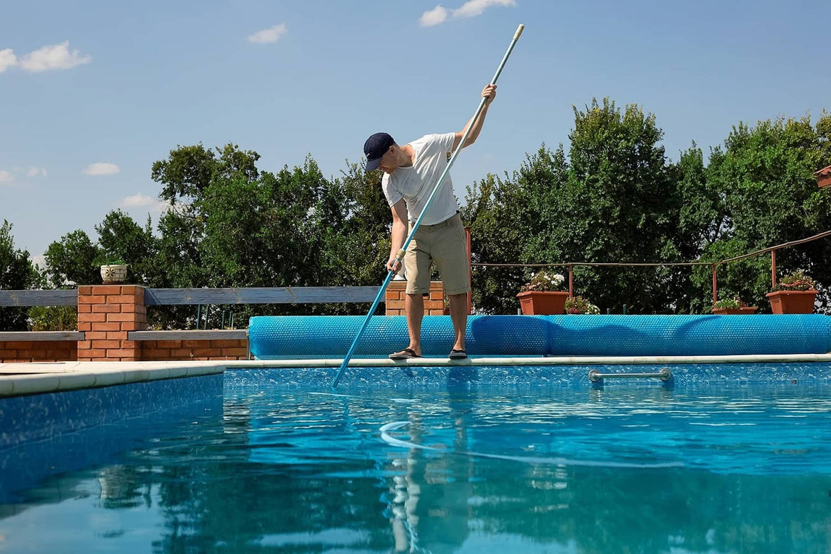 Blue telescopic pool pole used for backyard pool cleaning, held over the water