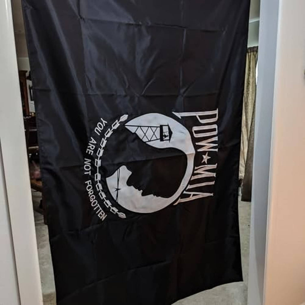 Double-sided POW-MIA flag close-up, black fabric with white profile emblem and text.