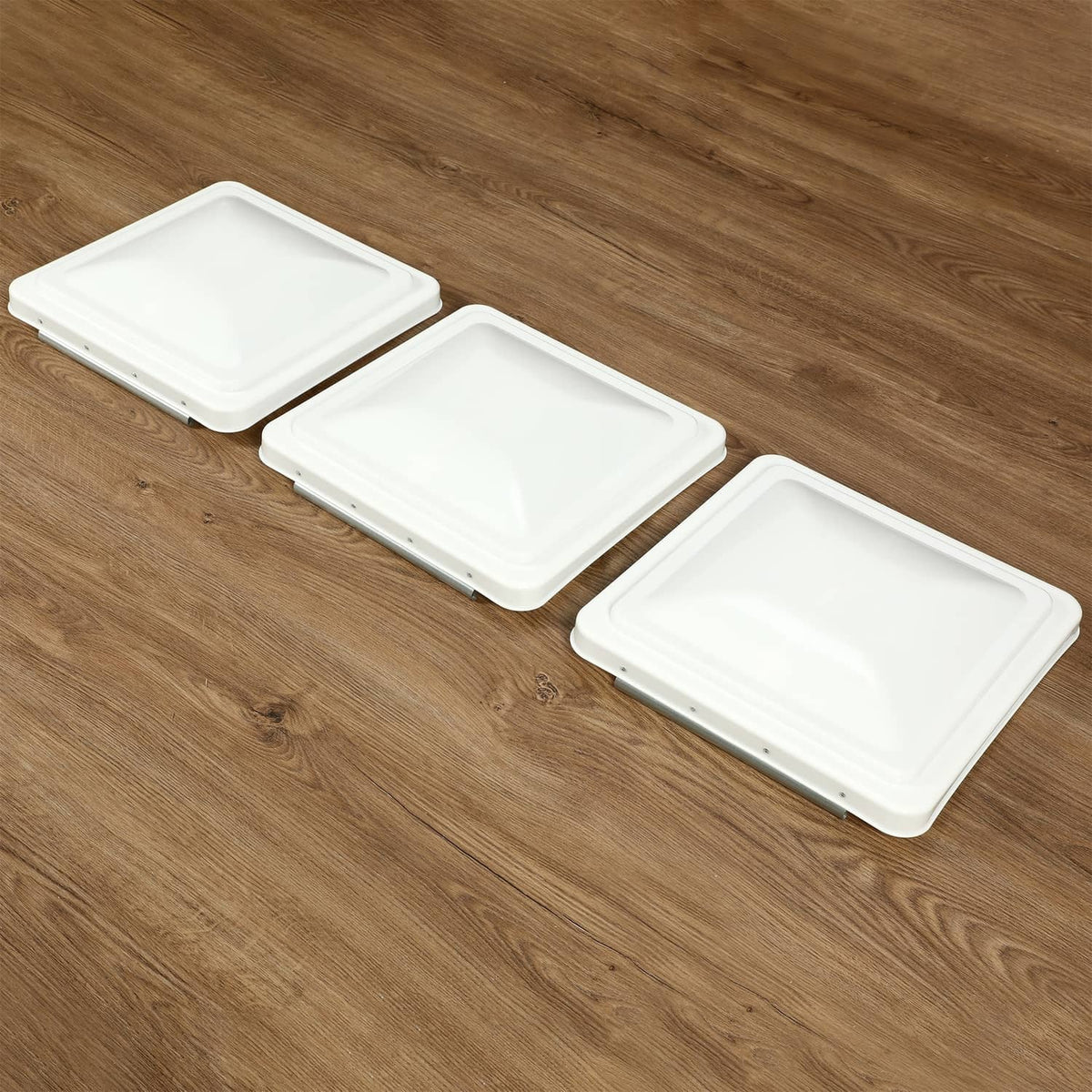 Three white RV roof vent covers arranged side-by-side on wood surface