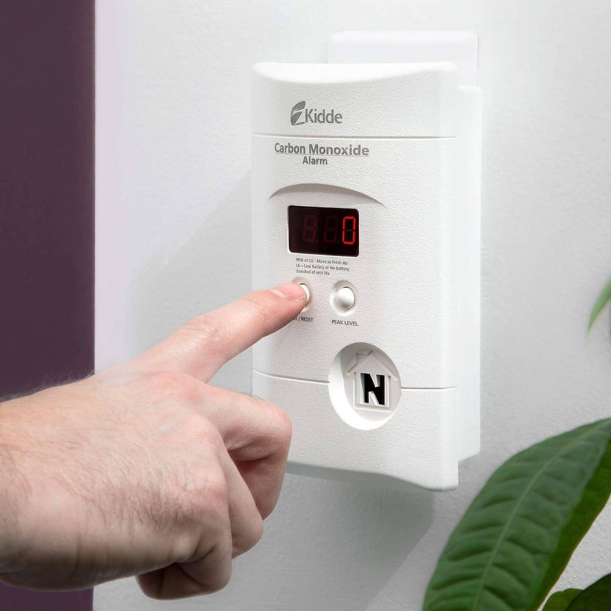 Kidde white carbon monoxide alarm with red digital display; hand pointing to controls