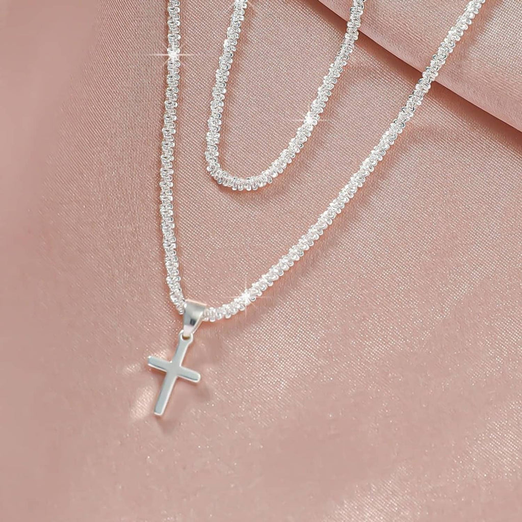Close-up of silver-tone cross charm pendant on layered chain links