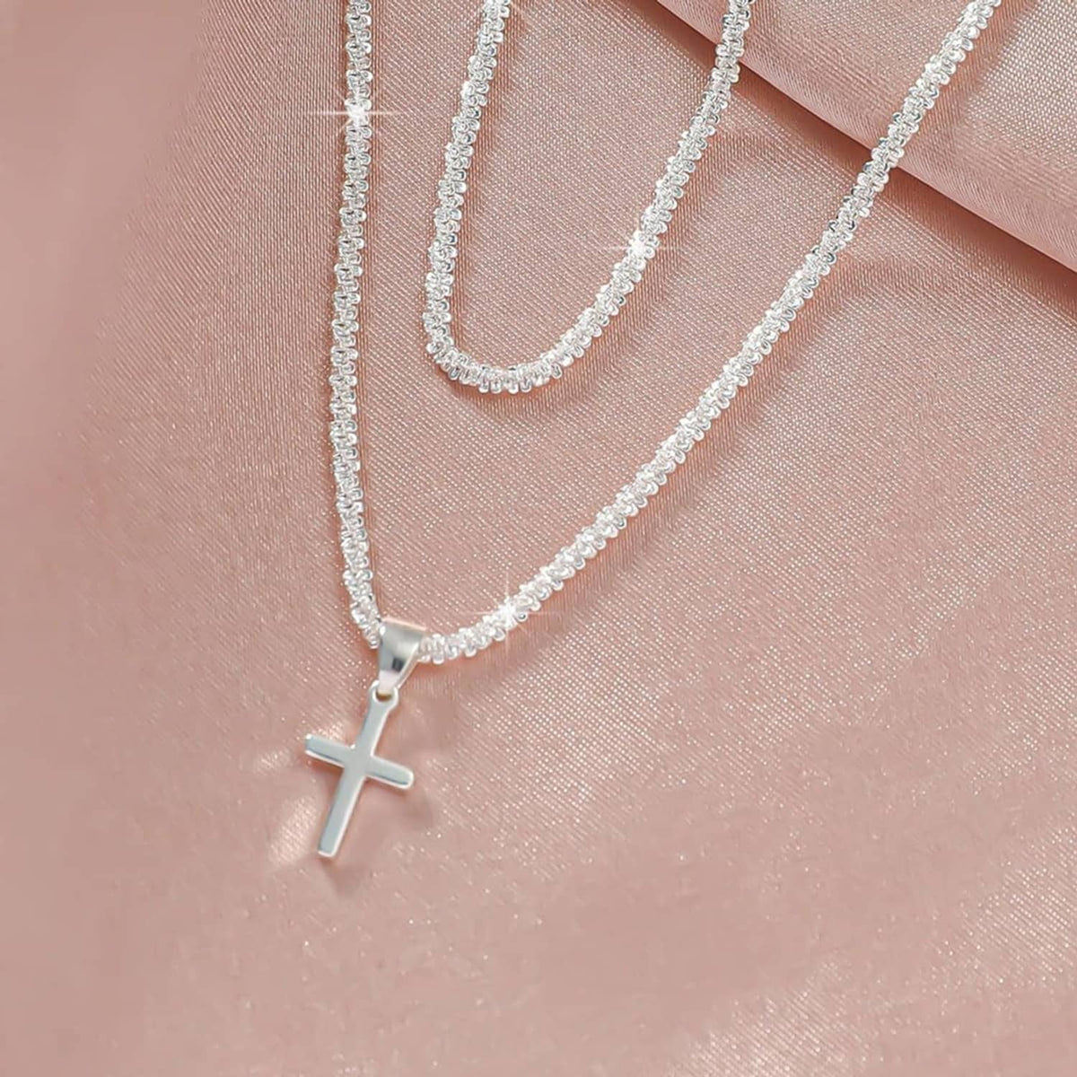 Close-up of silver-tone cross charm pendant on layered chain links