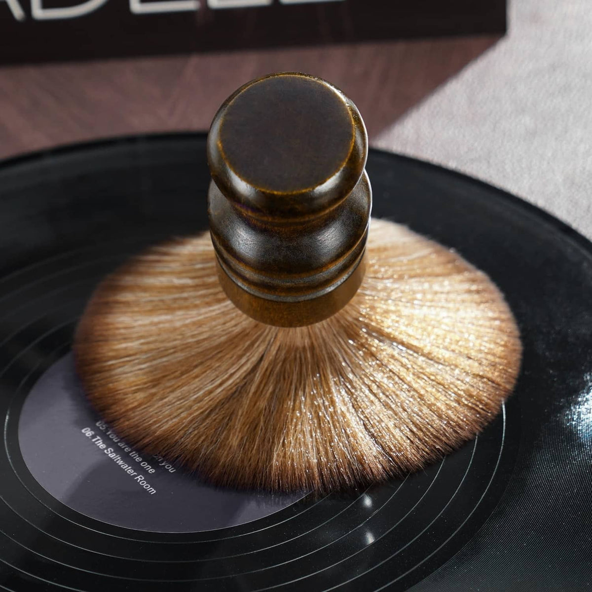 Wood-handled record cleaning brush sweeping soft brown bristles on vinyl