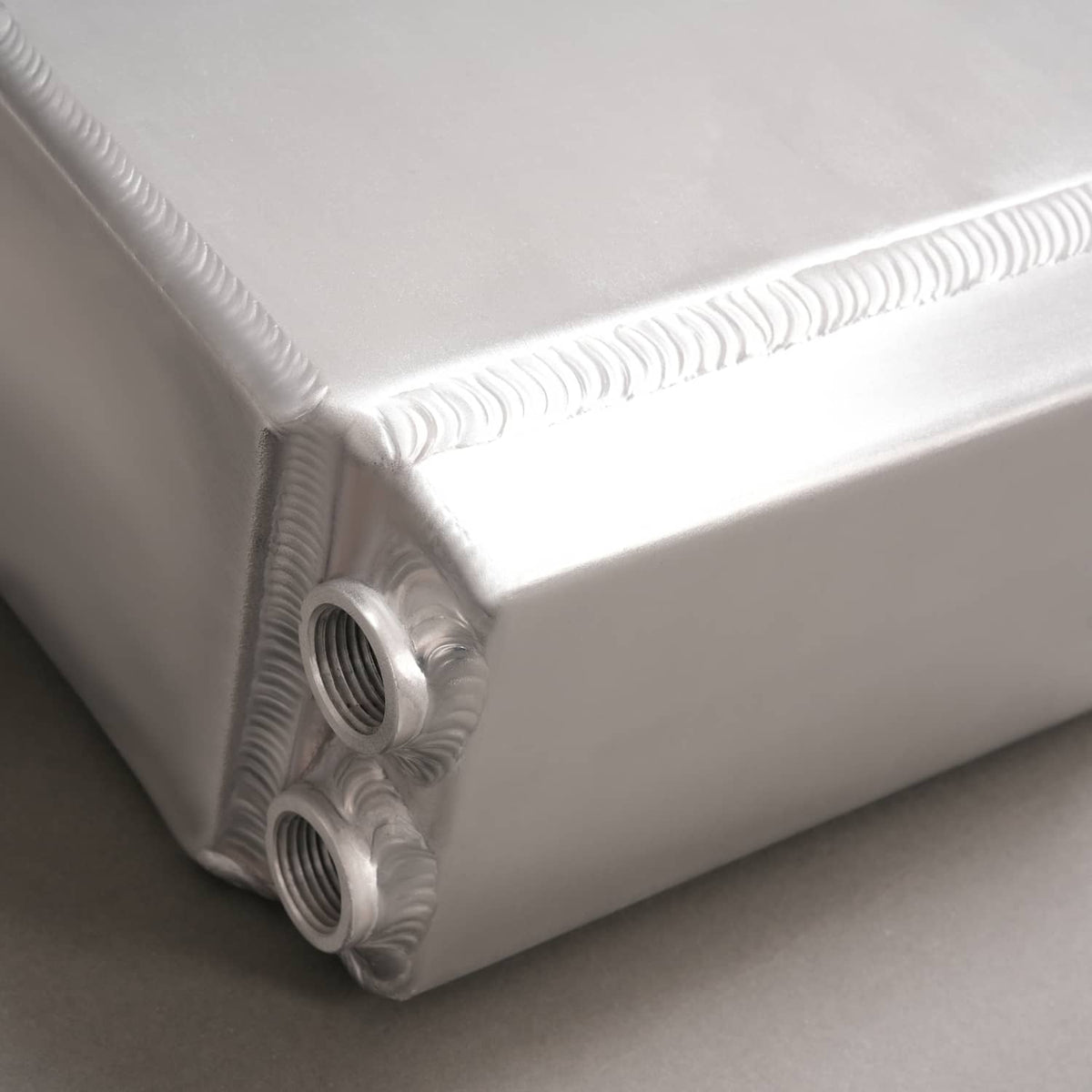 Aluminum intercooler end tank close-up with two threaded ports and cooling fins.