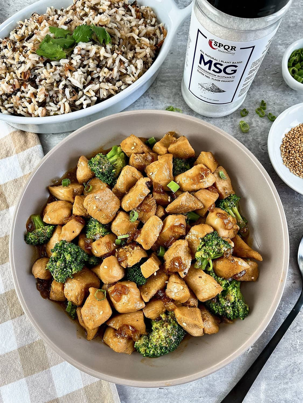 Chicken and broccoli bowl with MSG seasoning jar and grains on the side.