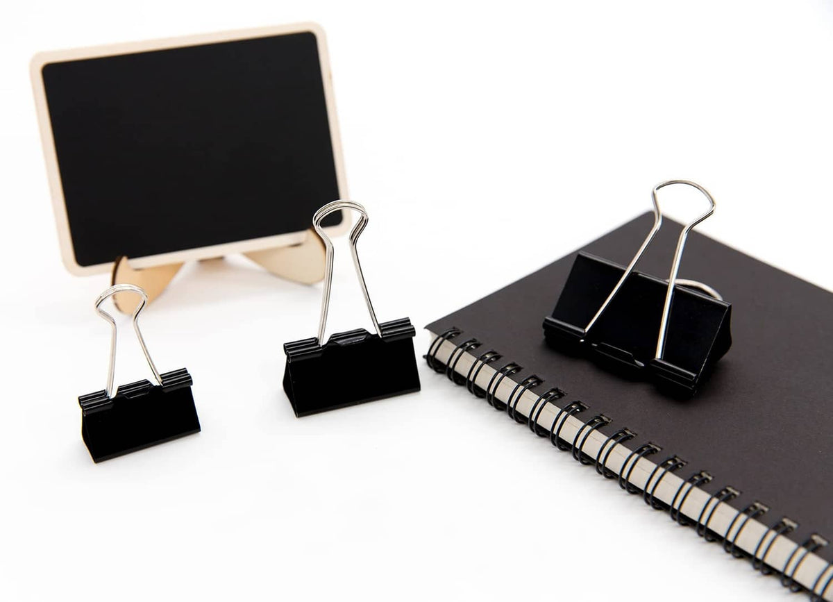 Black binder clips with metal wire loops holding papers, on office desk