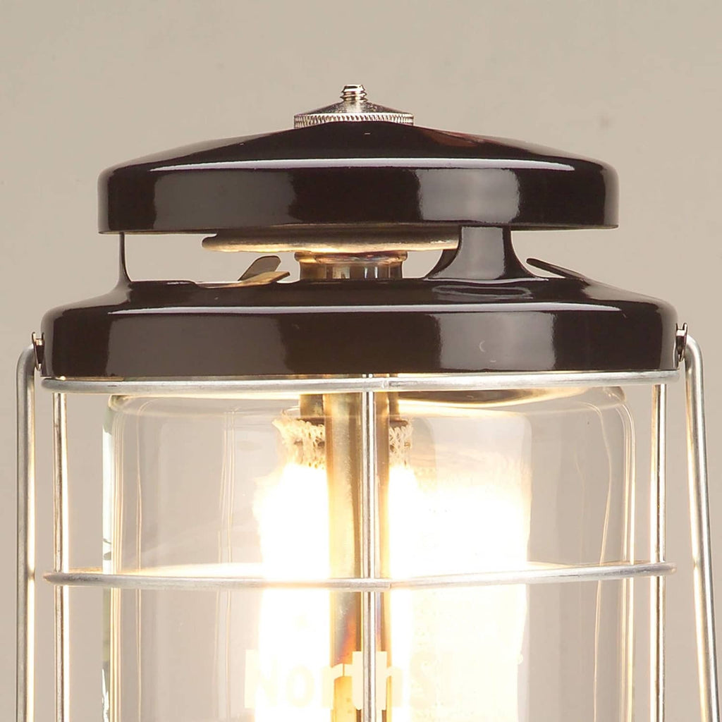 Coleman Northstar gas lantern top with black cap and clear glass chimney showing flame inside