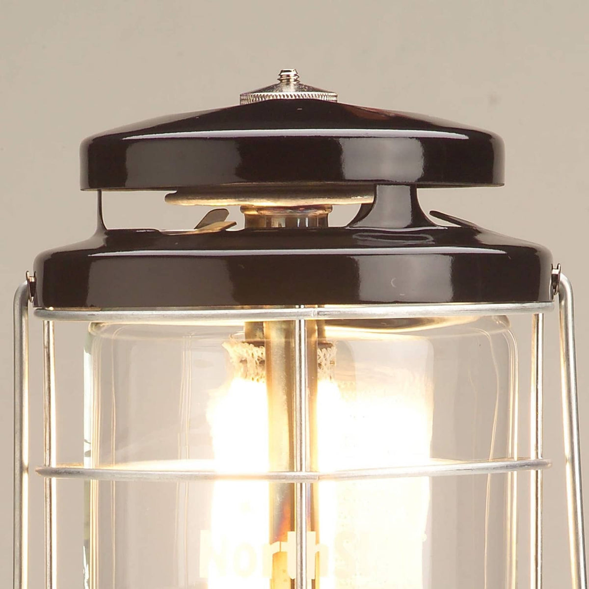 Coleman Northstar gas lantern top with black cap and clear glass chimney showing flame inside