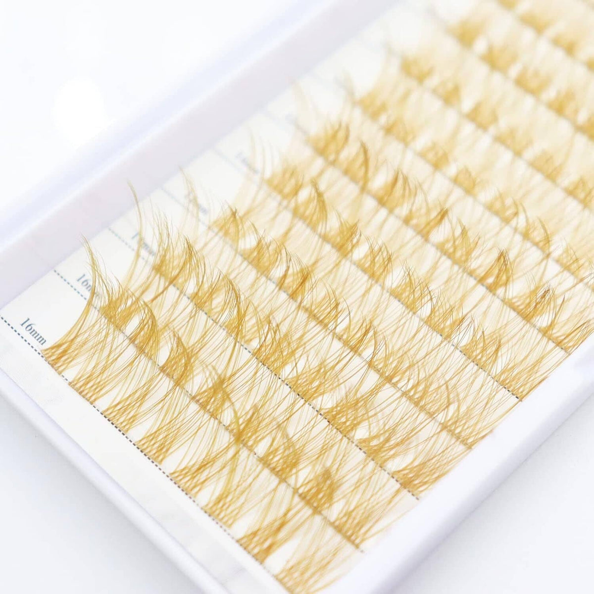 Close-up of gold-brown false lash clusters on a base sheet, arranged by length