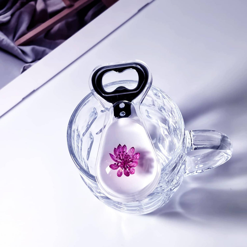 Resin bottle opener with clear handle, purple flower in body, black opener top
