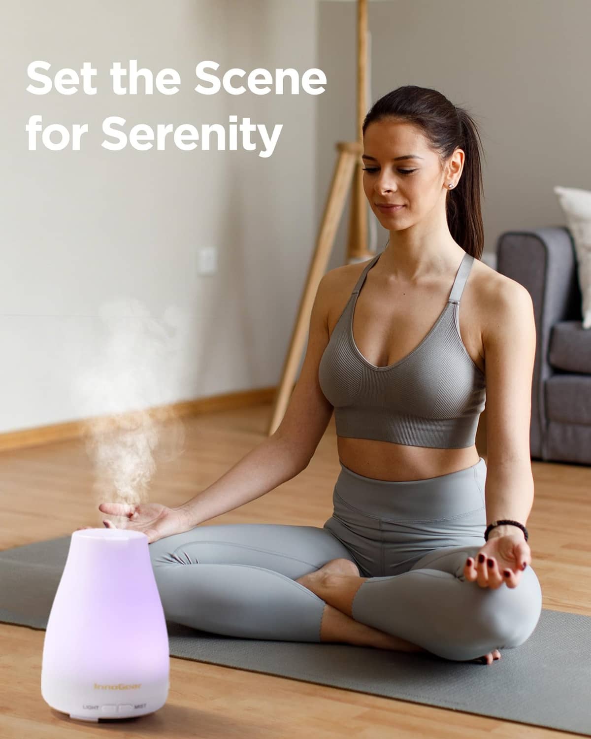 White essential oil diffuser releasing mist while person practices seated yoga