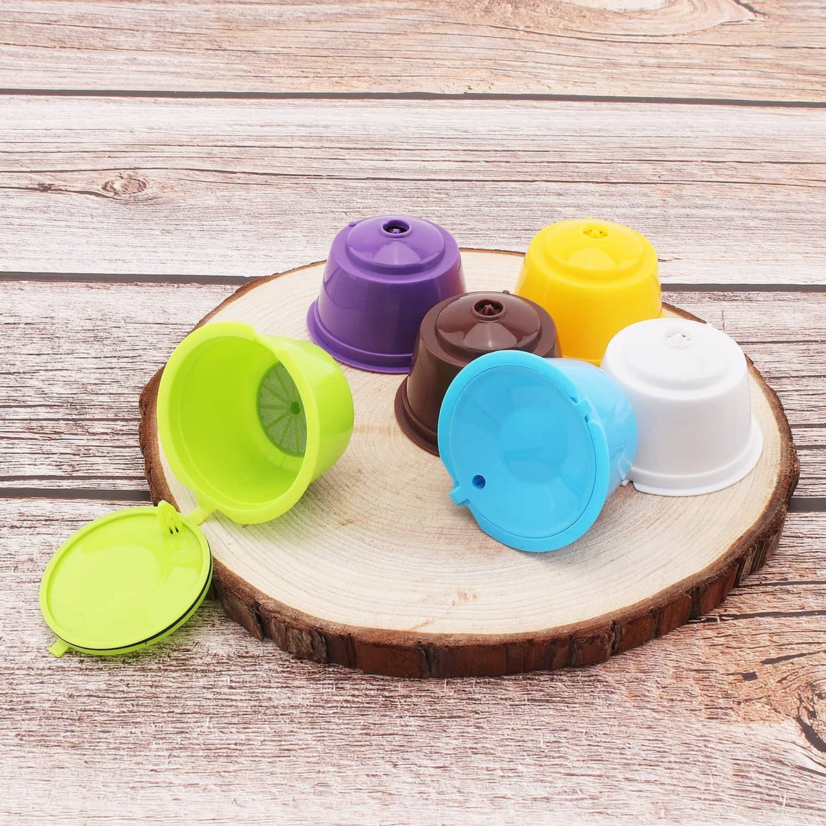 Six reusable coffee capsule lids in purple, yellow, green, blue, brown, and white on tray