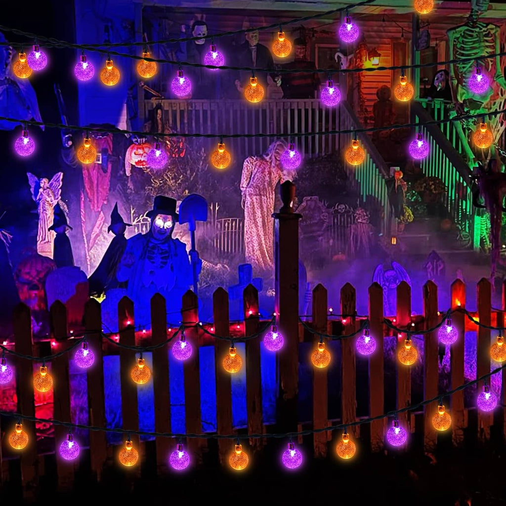 Halloween solar string lights with orange and purple globe bulbs along a yard fence.