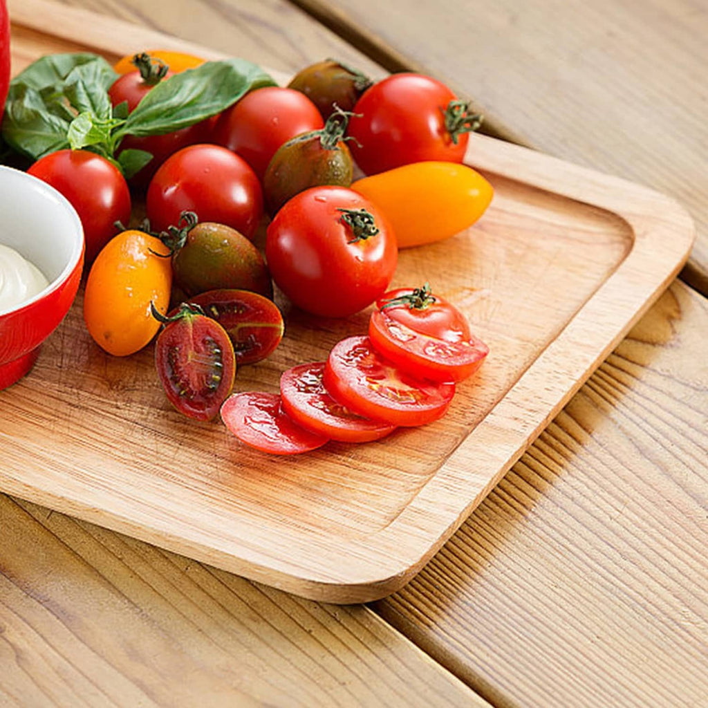 Wooden cutting board with tomatoes and tomato slices on a kitchen table