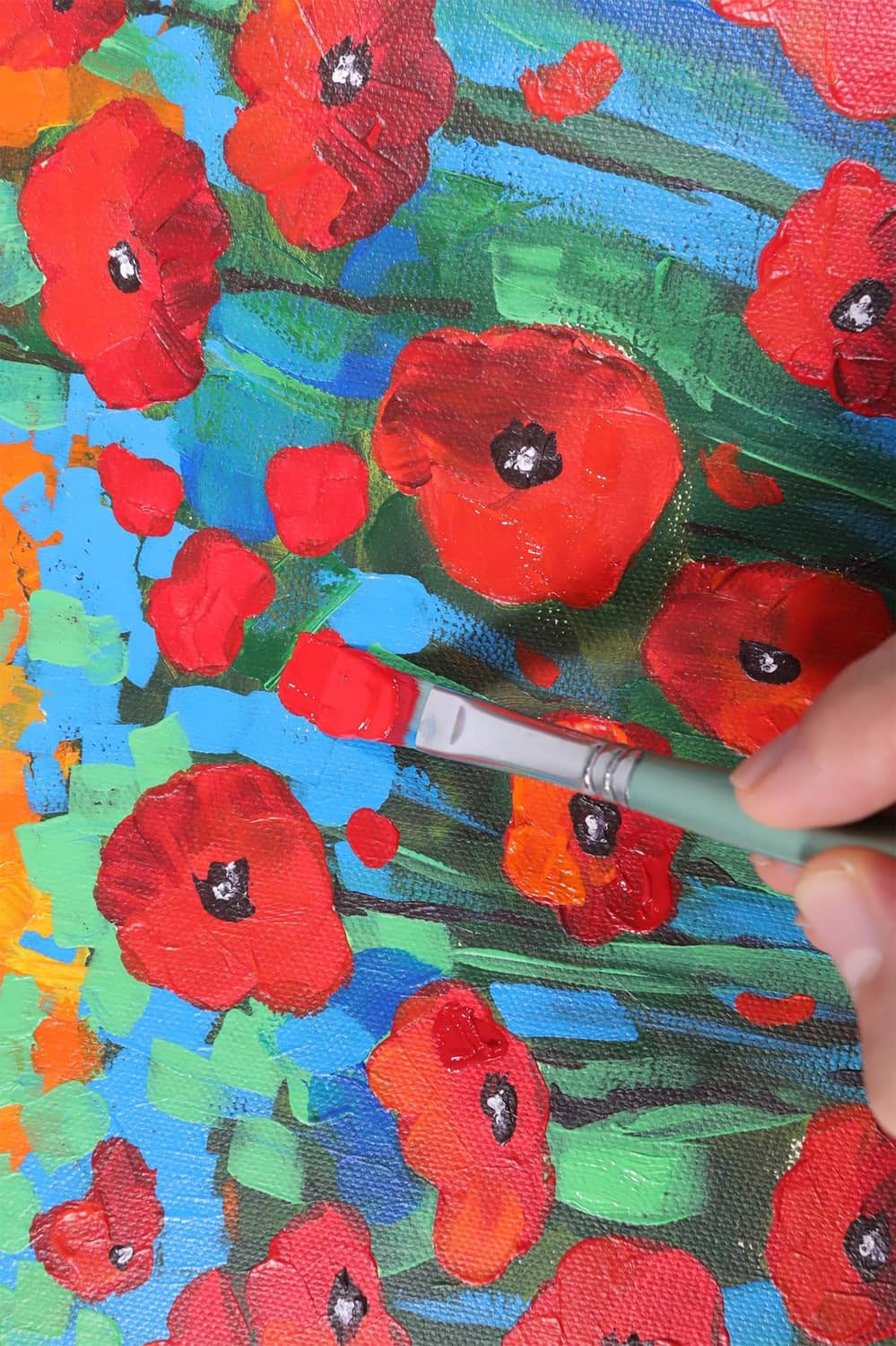 Hand painting a canvas with red flower shapes and visible acrylic brush strokes