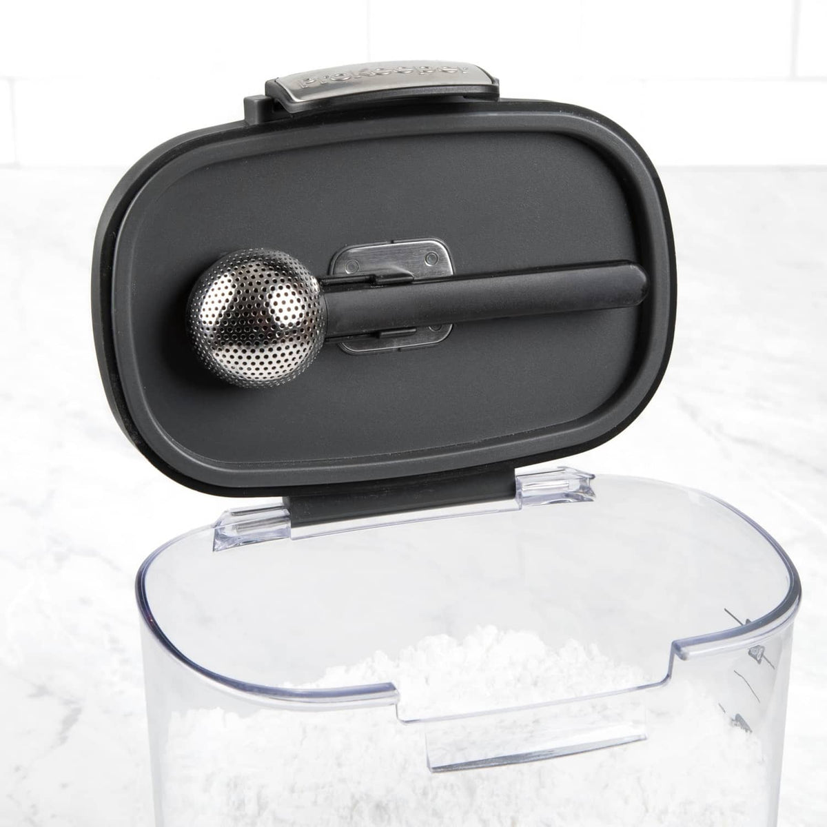 Clear airtight food storage container with black lid and perforated metal scoop insert