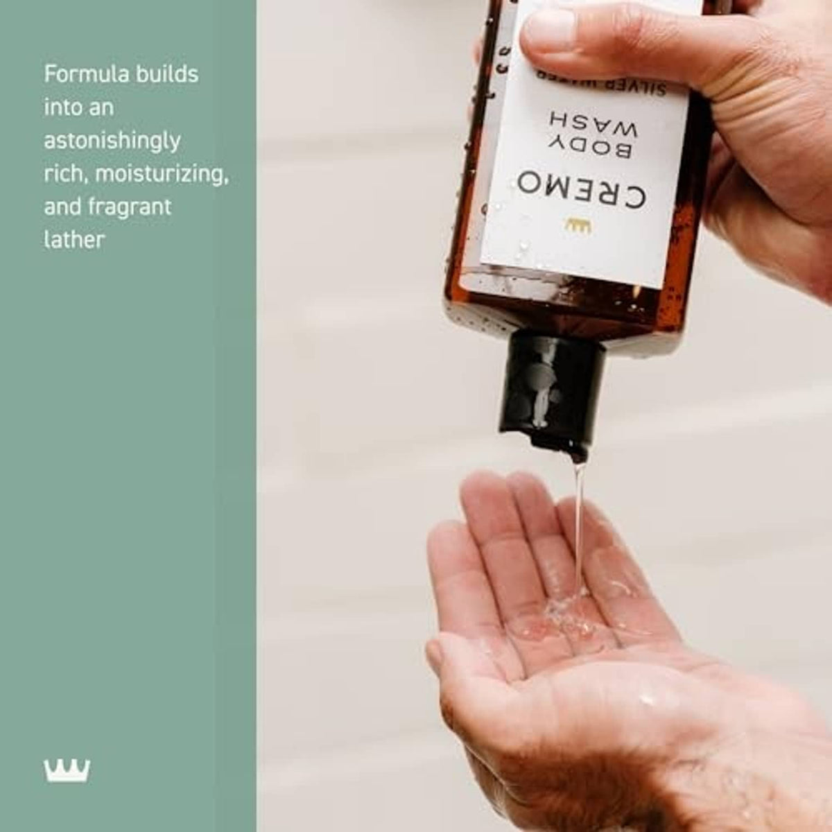 Hands squeezing Cremo body wash into open palms, amber bottle, black cap