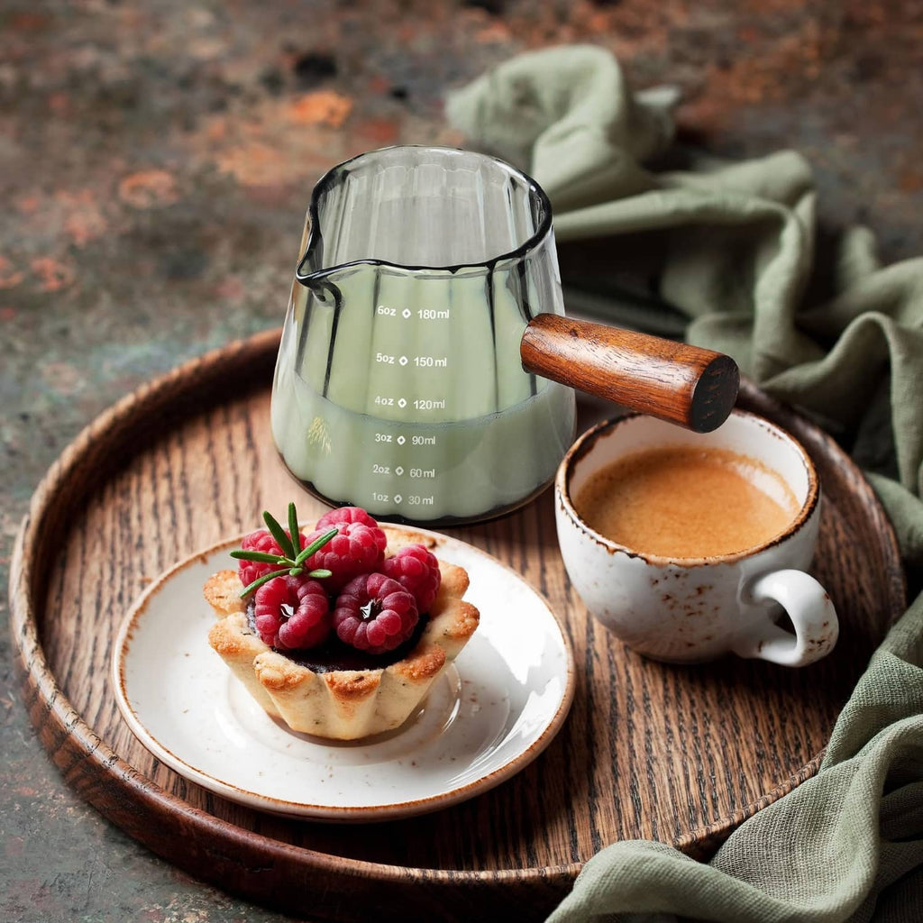Clear single-spout measuring cup with wood handle and ml markings on a serving tray