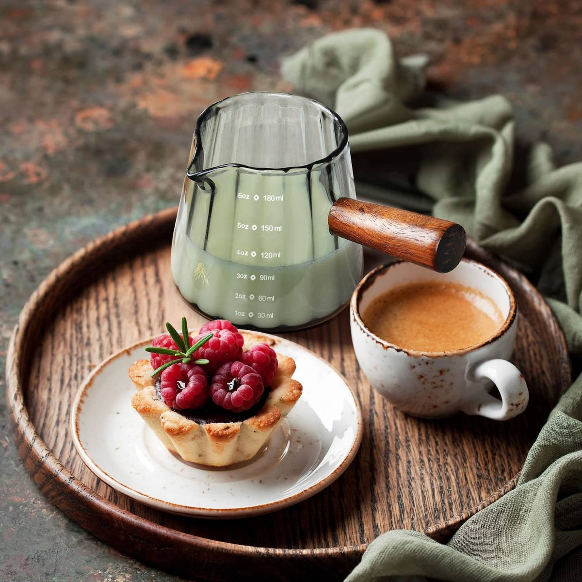 Clear single-spout measuring cup with wood handle and ml markings on a serving tray