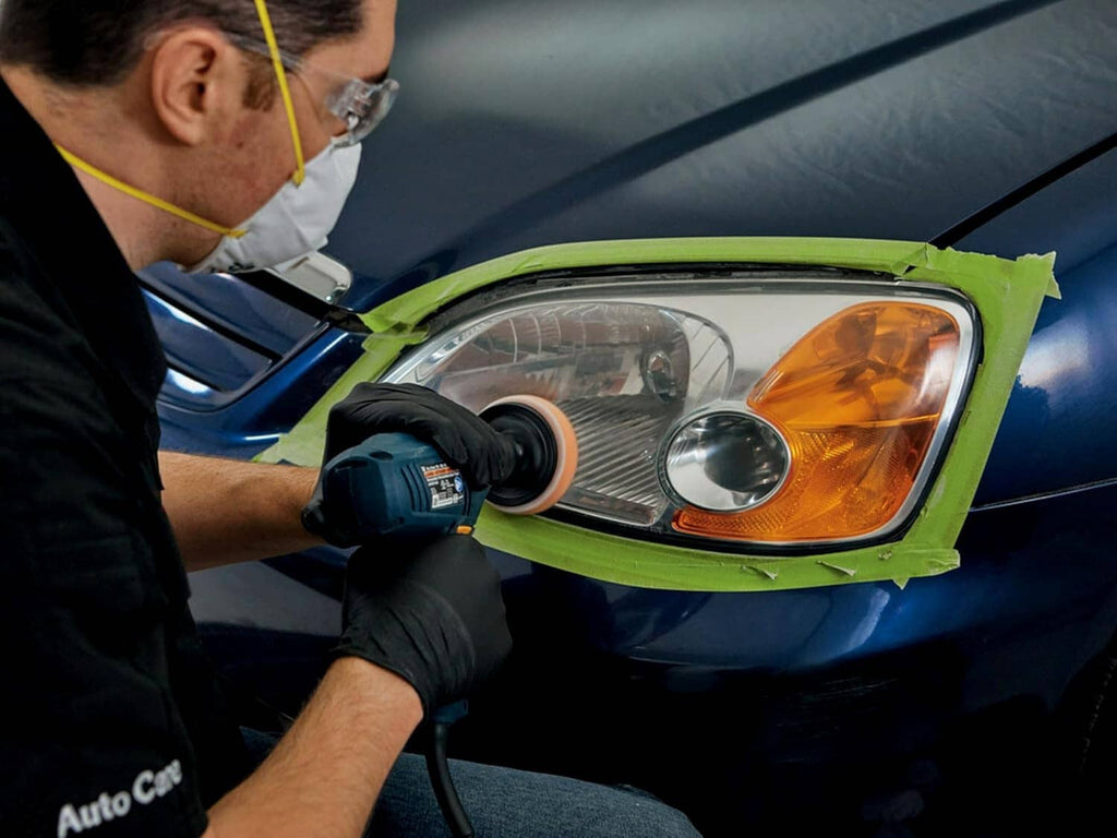 Auto technician restores a headlight with a power tool under green masking tape
