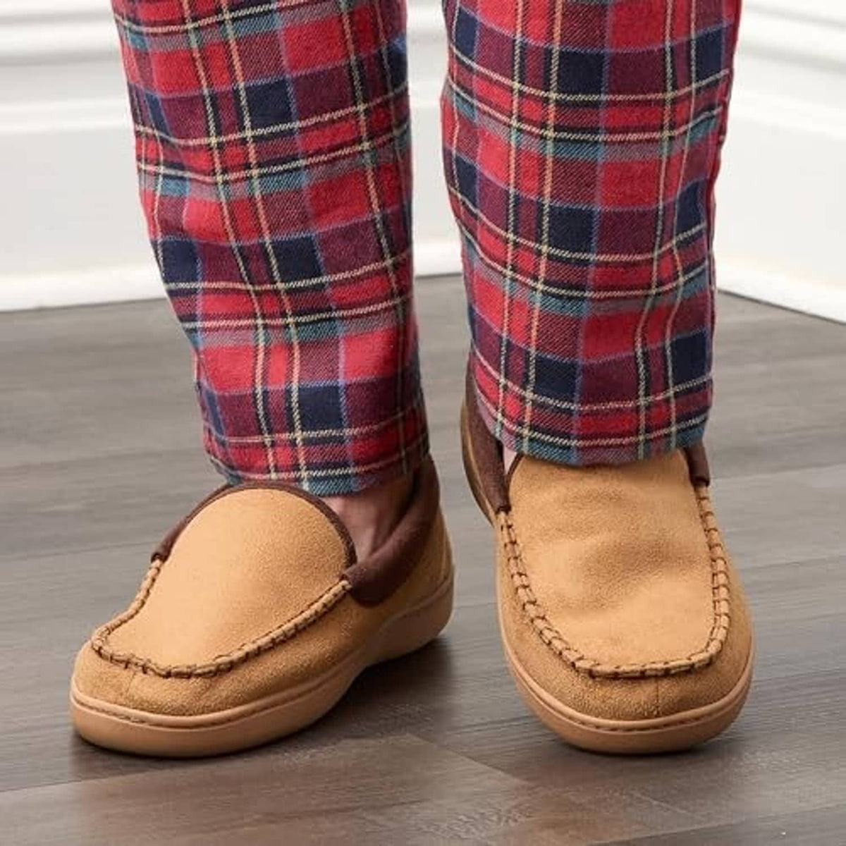 Tan slip-on slippers on wood floor with plaid pants cuffs above the openings