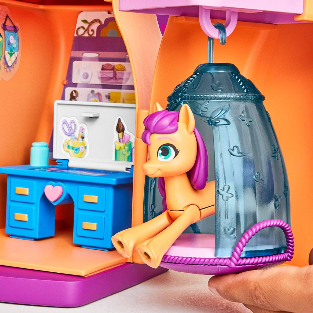 Unicorn doll holding onto a blue swinging bag accessory beside the playset kitchen