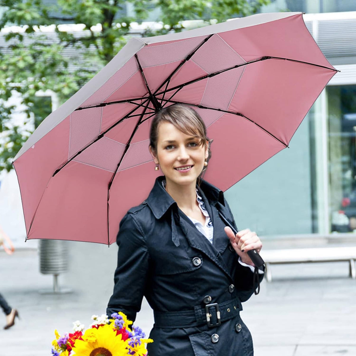 Pink travel umbrella held by a person in outdoor street setting