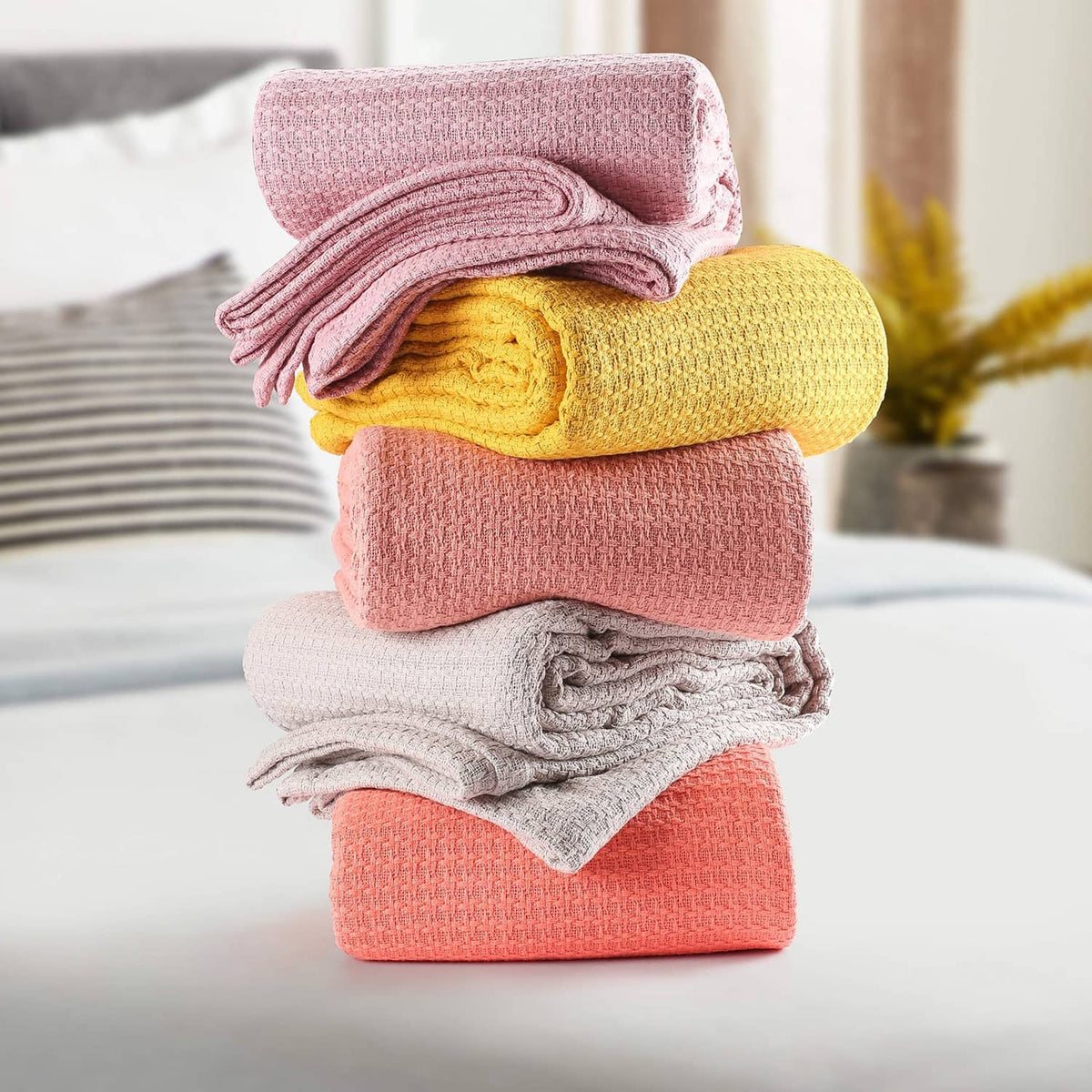 Stack of folded bed blankets in pink, yellow, coral orange, gray.