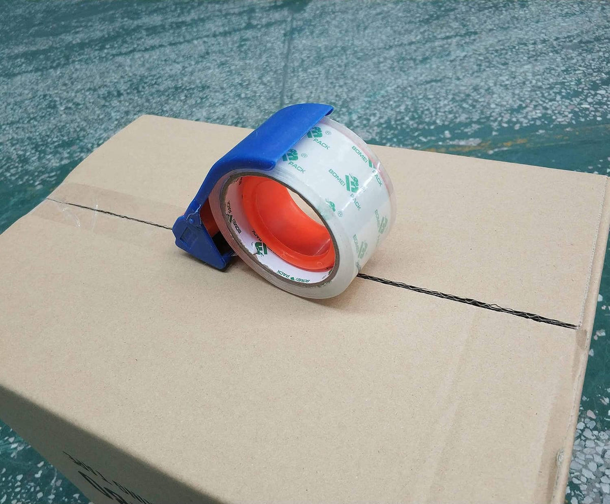 Clear packing tape roll on blue dispenser, applied across a cardboard box seam