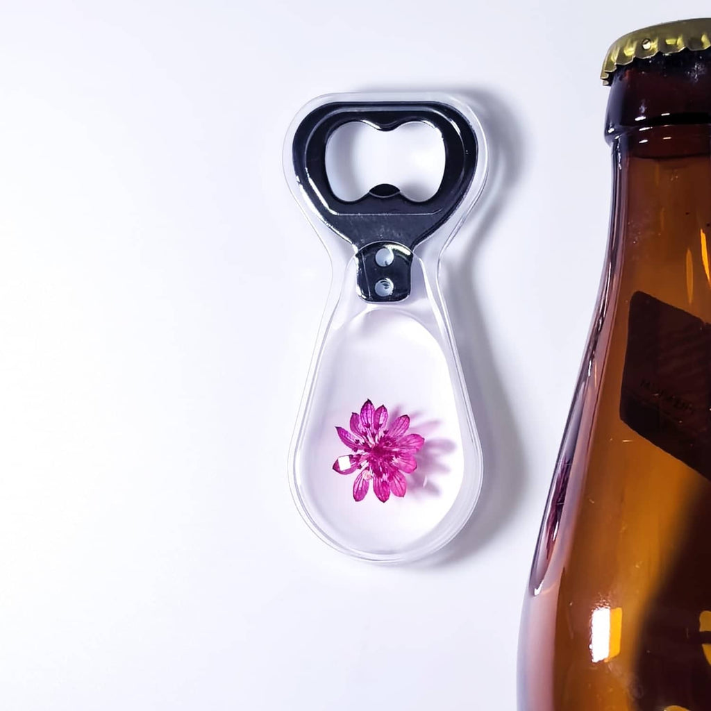Resin bottle opener with clear body and purple flower under black opener head