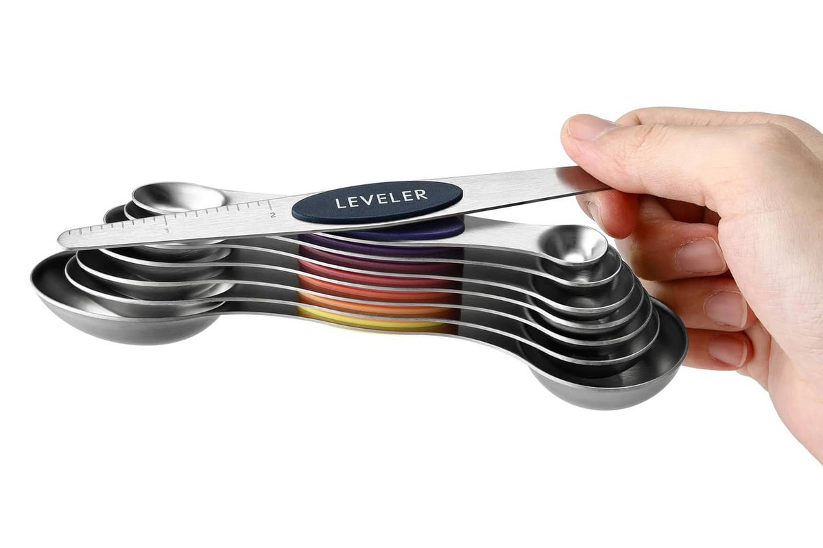 Hand holding nested stainless steel magnetic measuring spoons with lever bar