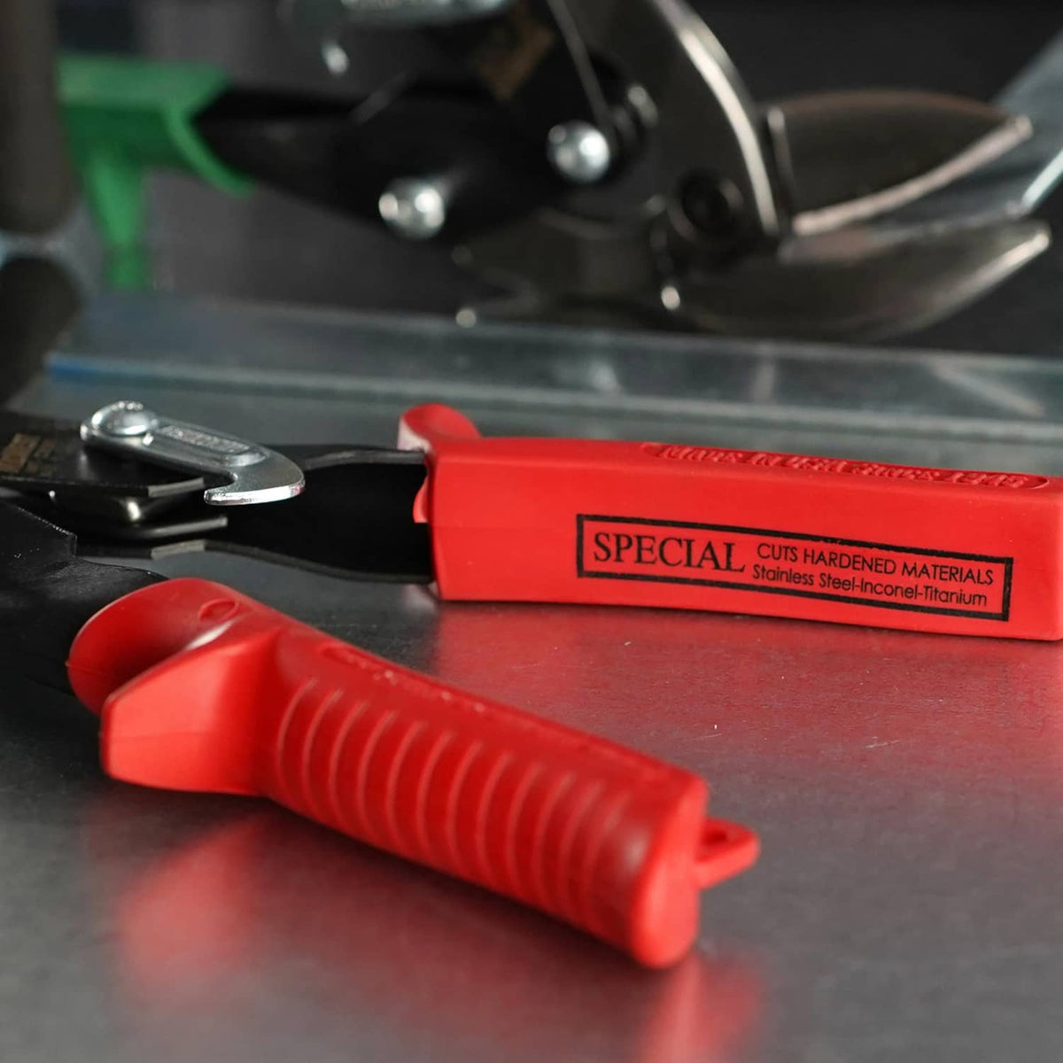 Aviation snips shown with red handle on a work surface near metal sheet