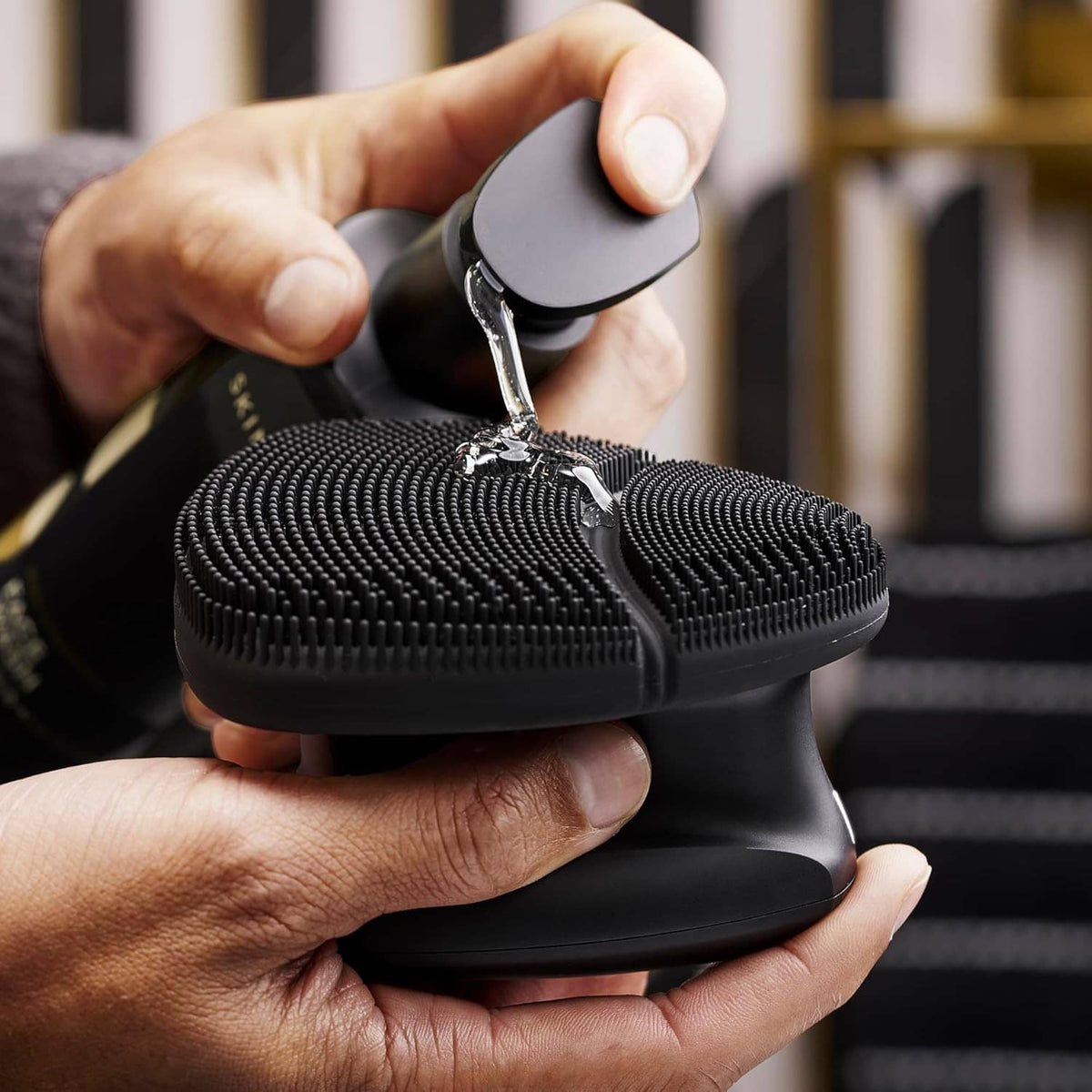 Hands holding electric silicone face scrubber; water drips from the bristles