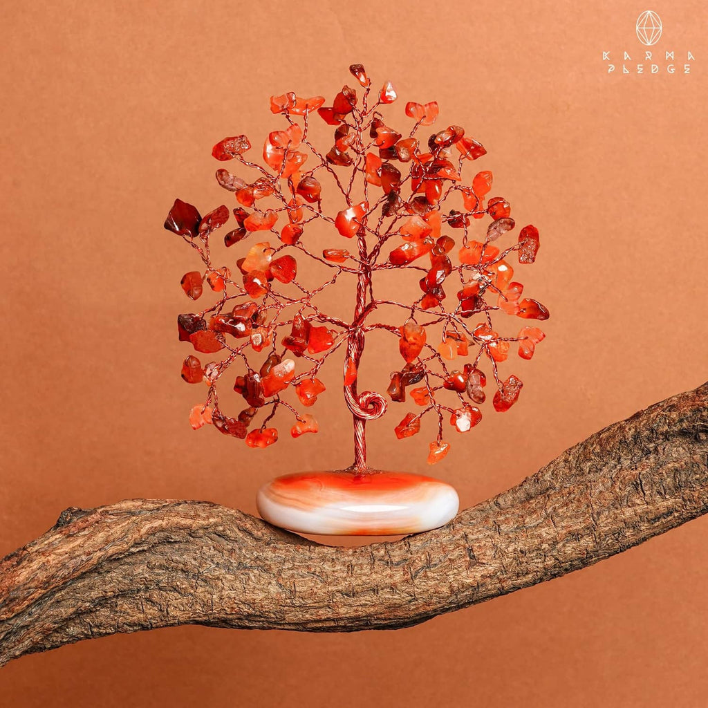 Orange-red carnelian crystal tree on white palm-stone base perched on natural wood