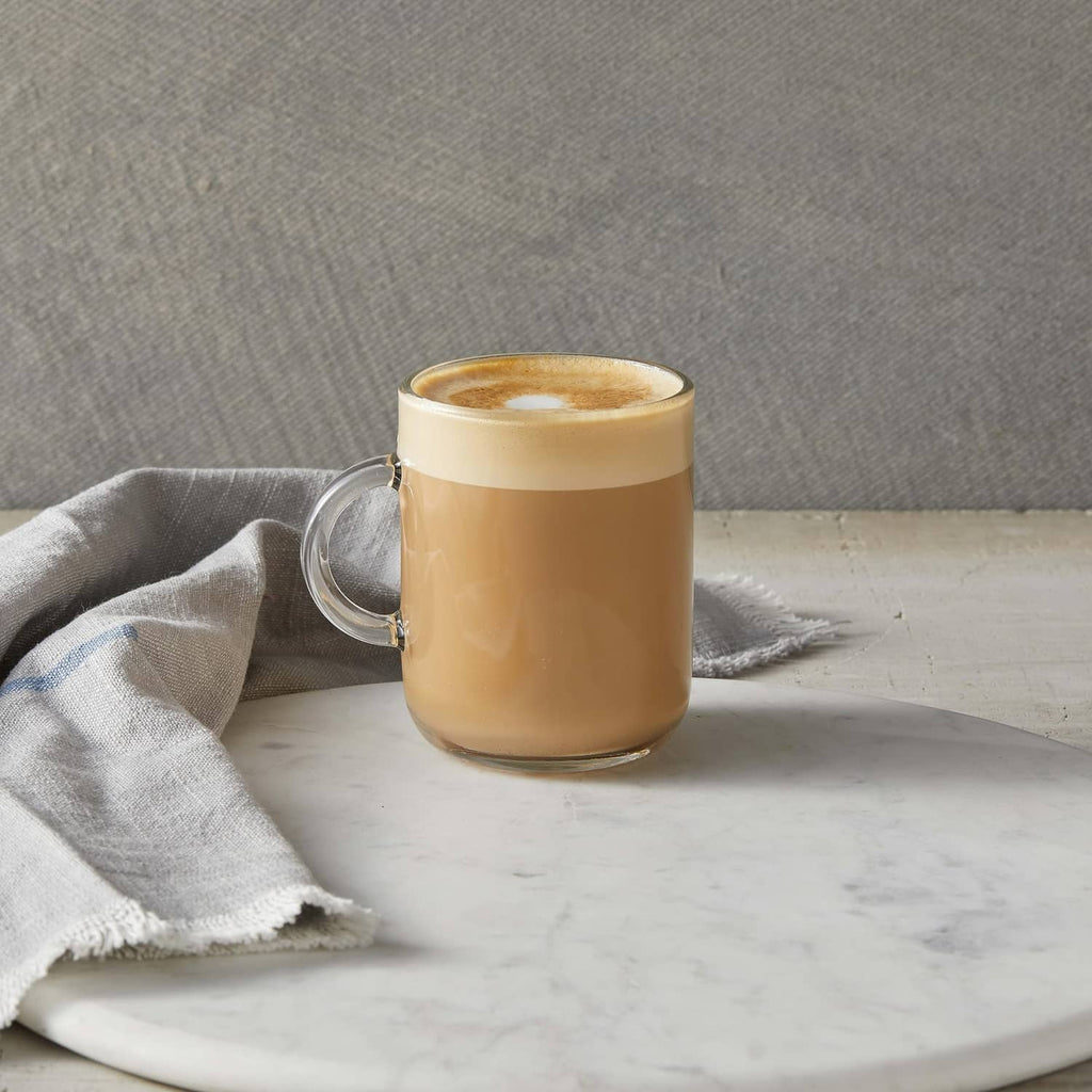 Glass latte mug filled with creamy tan syrup drink and foam top