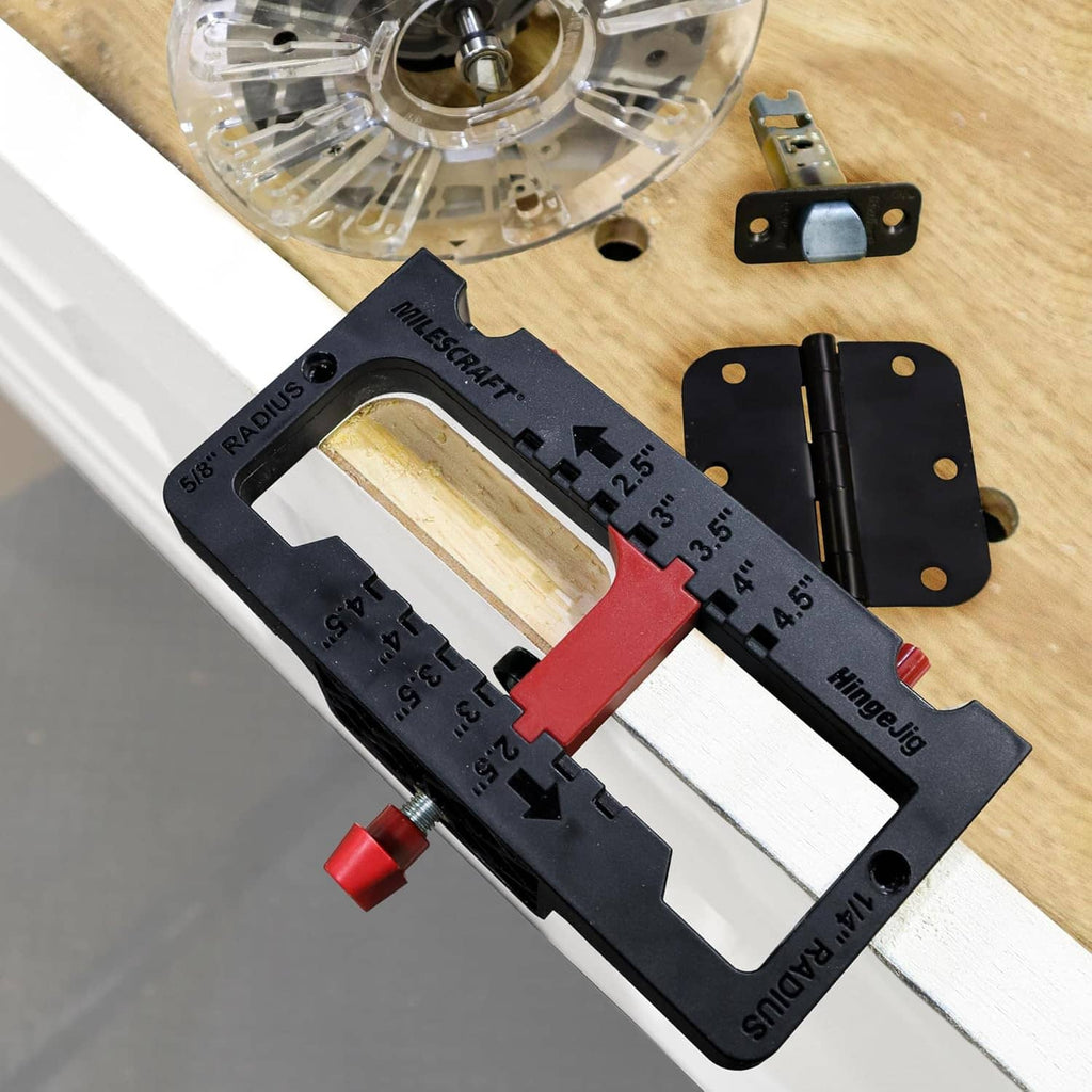 Hinge jig with red clamp, hinge bit, and black hinge plates on a work surface