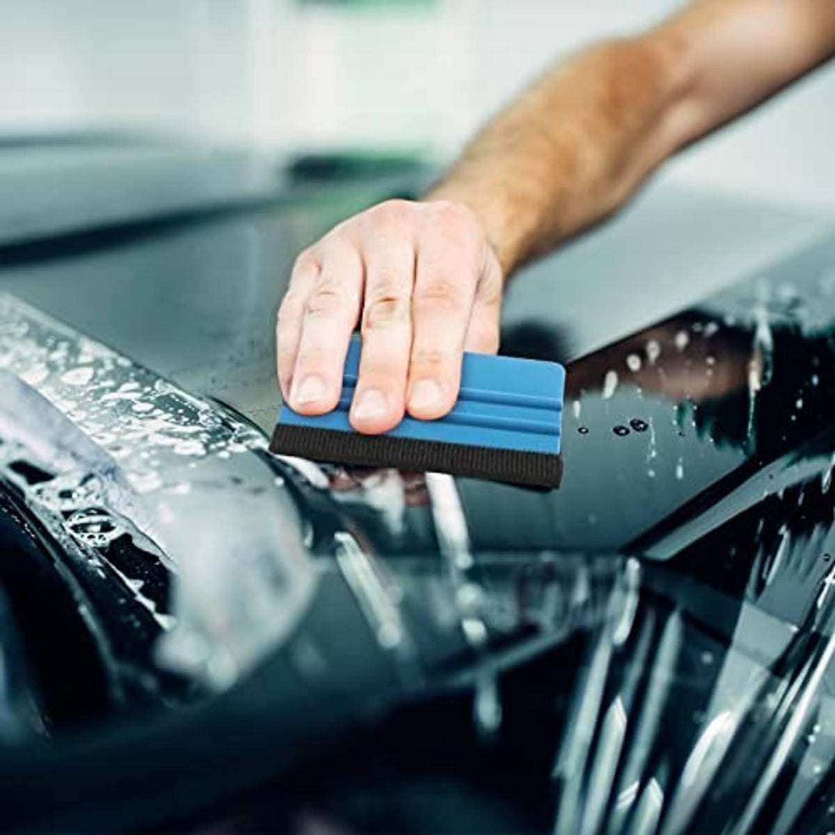 Blue vinyl squeegee with black felt edge, smoothing clear film on glass