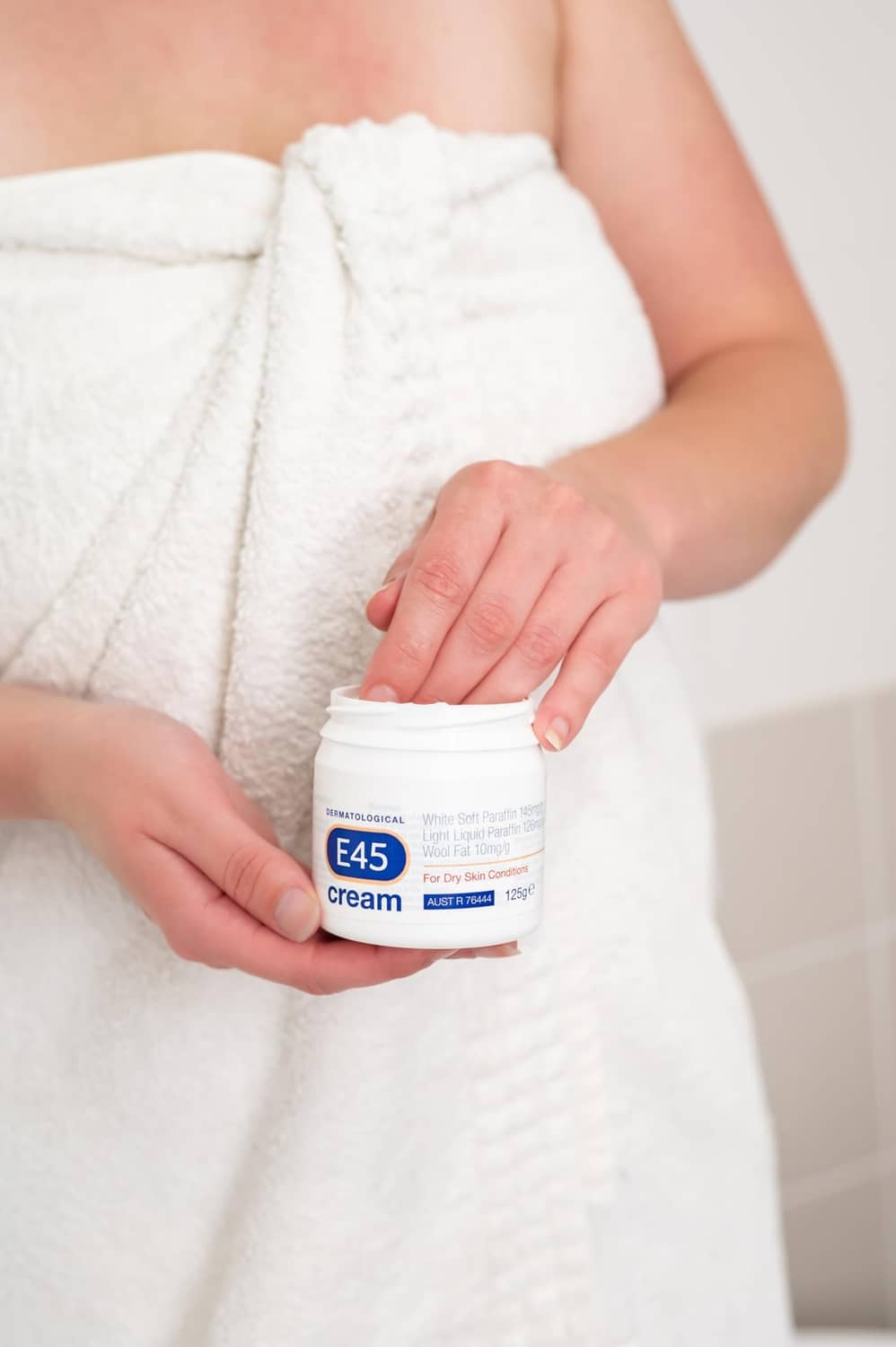 Person holding E45 dermatological cream jar while wrapped in a towel