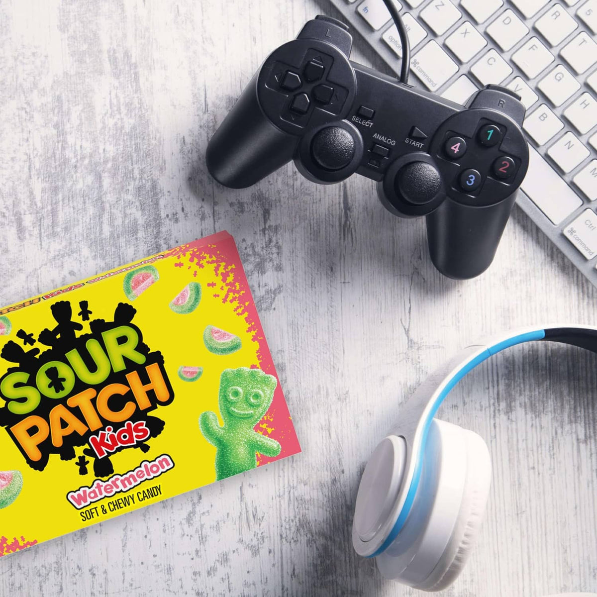Sour Patch Kids candy box next to black game controller and over-ear headset