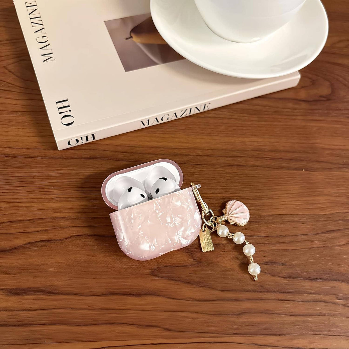 Pink glitter TPU AirPods case with pearl keychain charm, earbuds visible on wooden surface