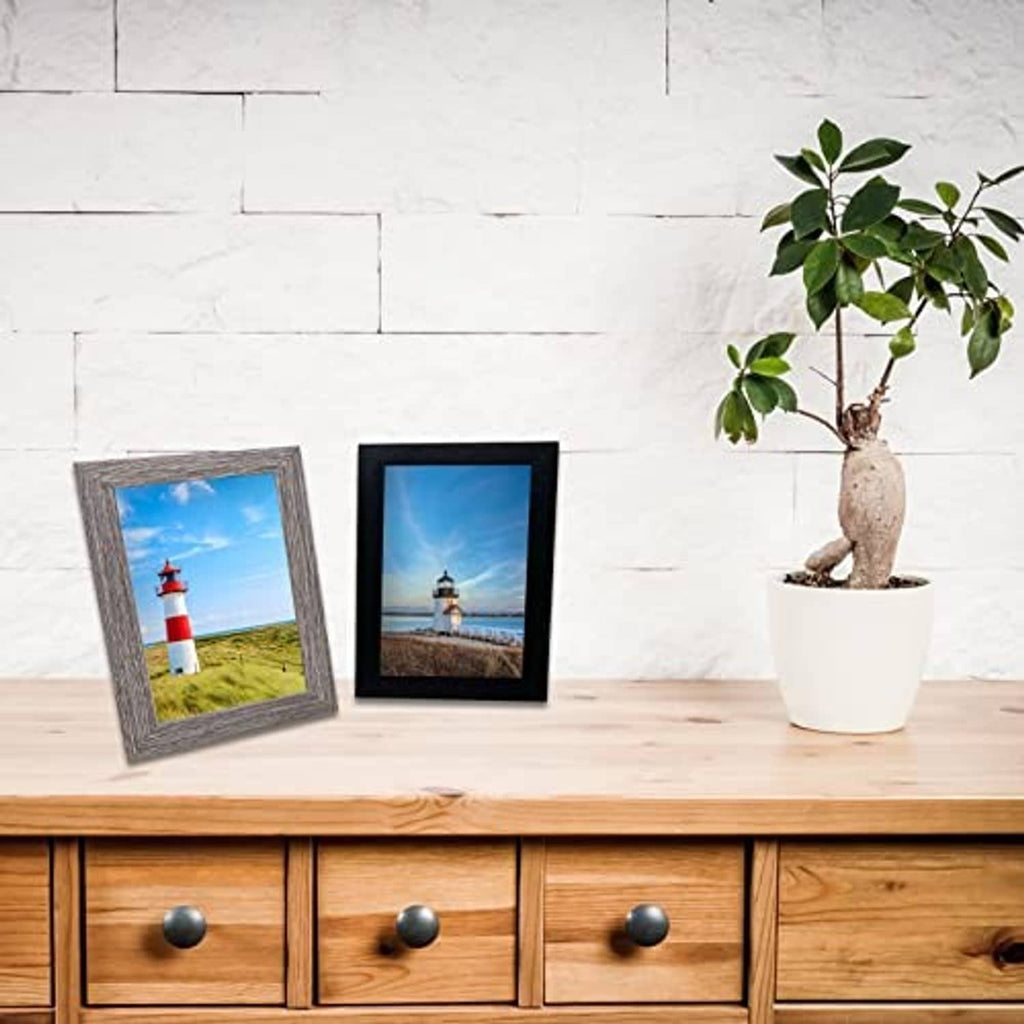 Two small photo frames on a wooden shelf with lighthouse and coastal scene prints