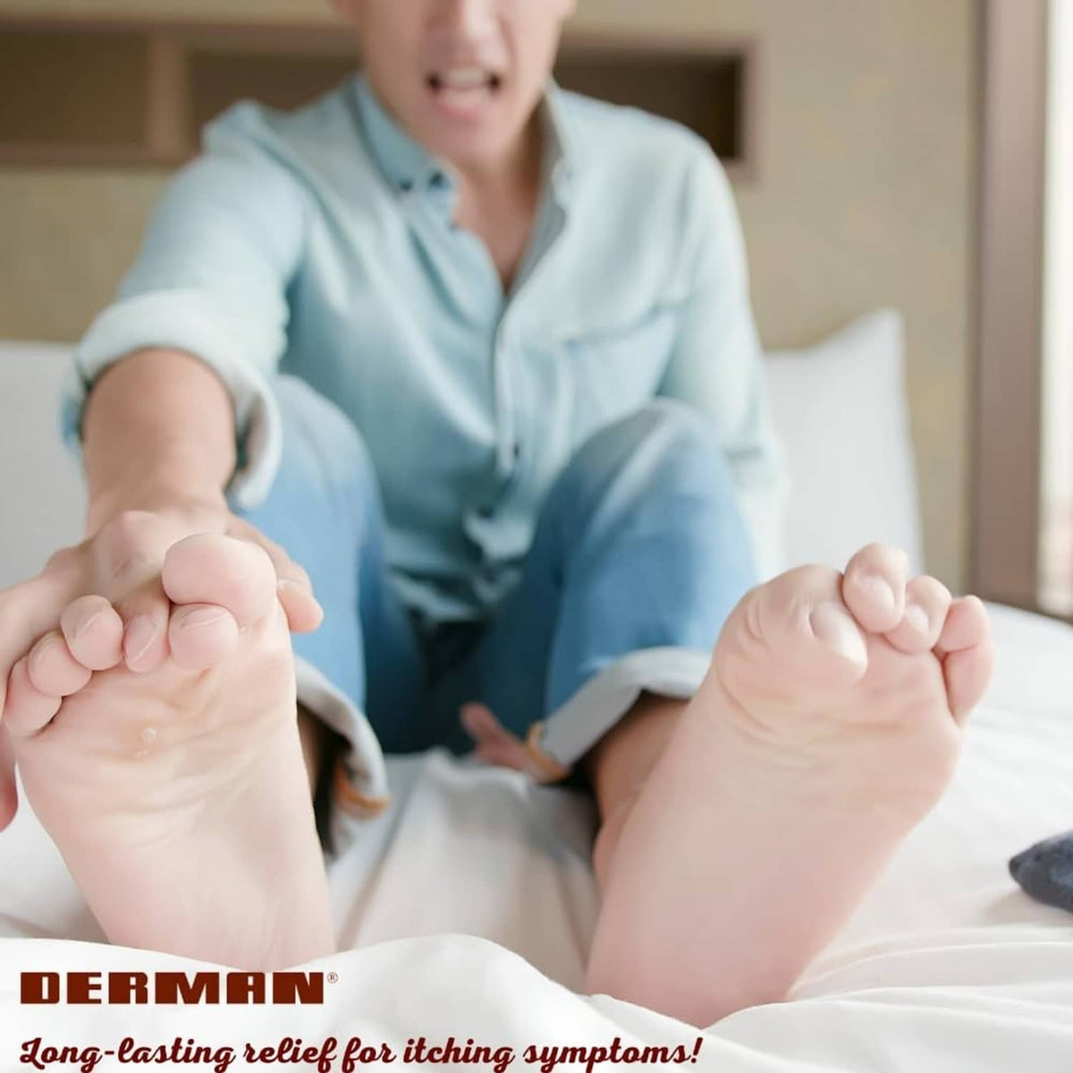 Person applying Derman antifungal cream to feet while relaxing on a bed.