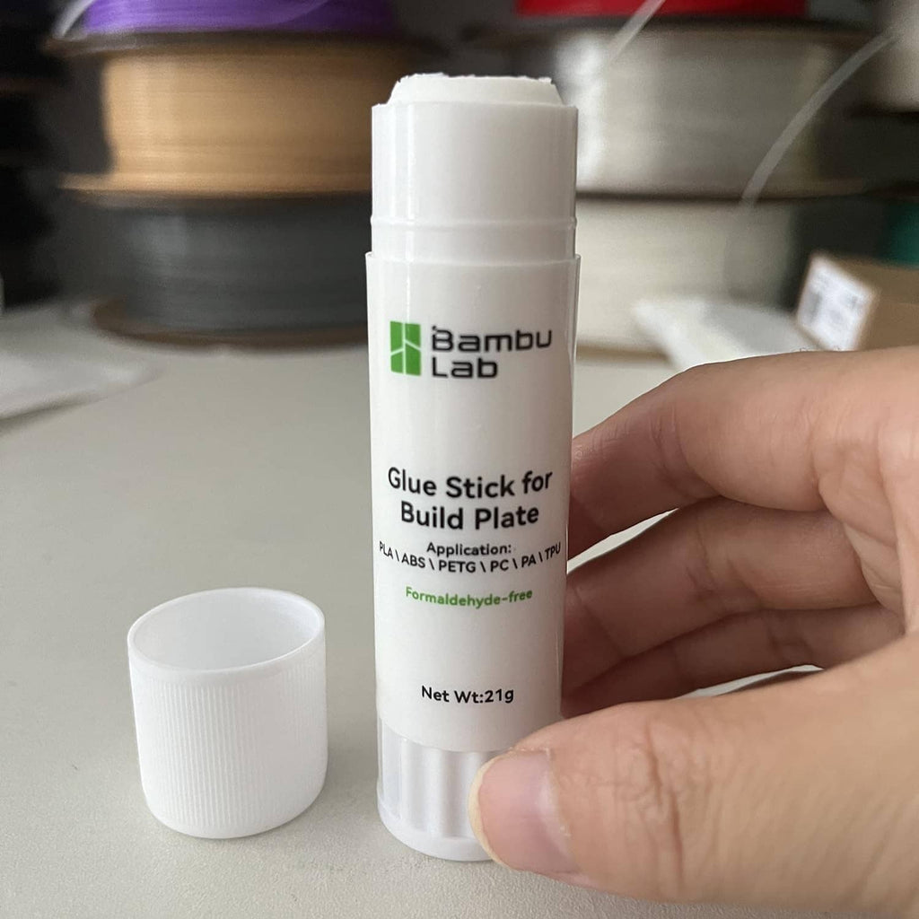Bambu Lab glue stick for build plate, bottle held by hand with small stick cup