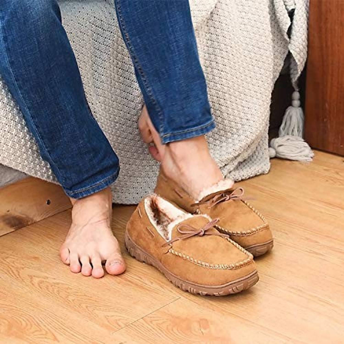 Brown moccasin slippers with plush lining worn by person on wooden floor