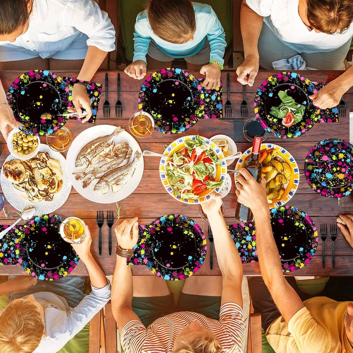 Neon splatter glow plates and napkins held by guests around a party table