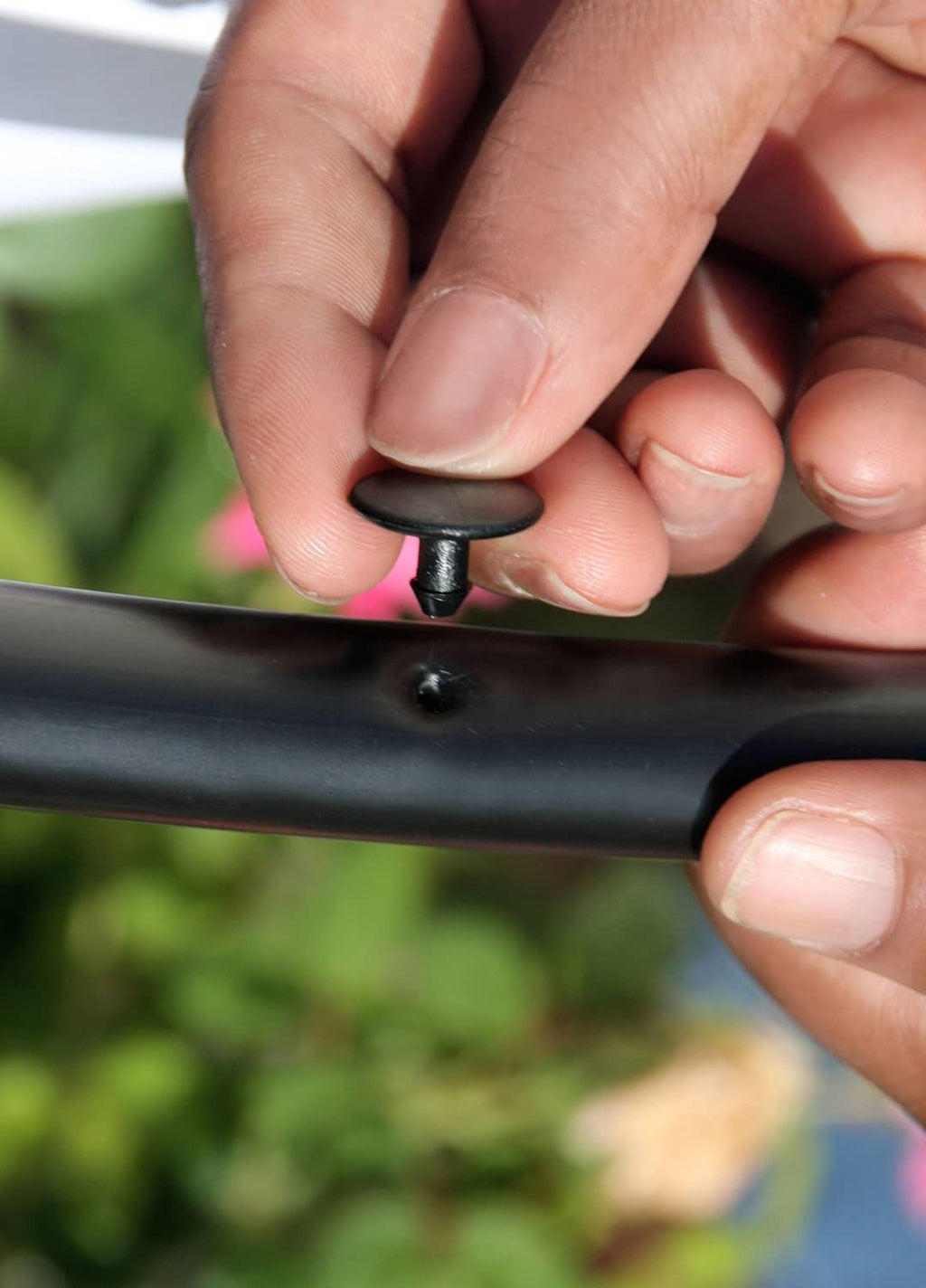 Black goof plug inserted into drip tubing hole, held by hands