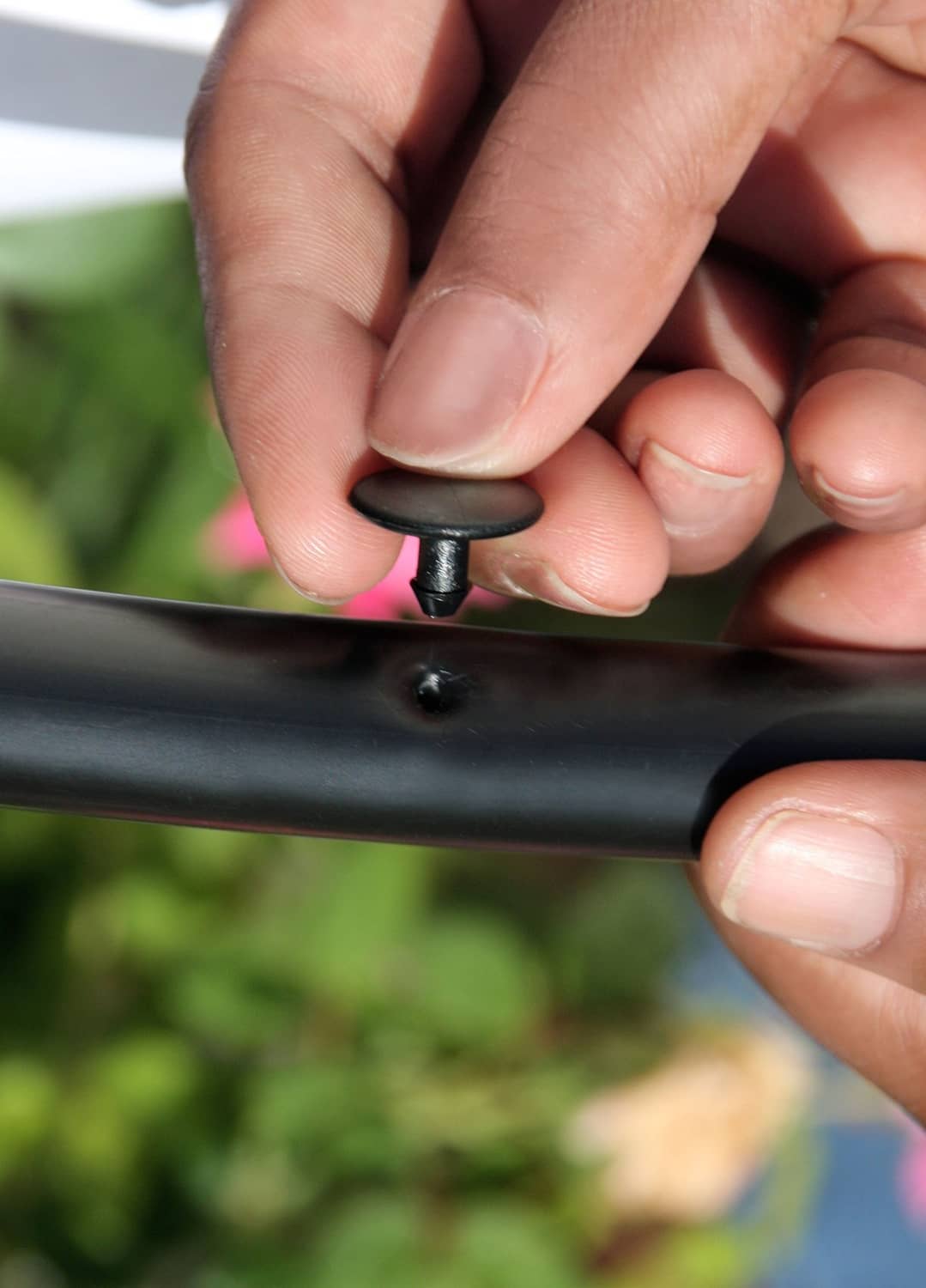 Black goof plug inserted into drip tubing hole, held by hands