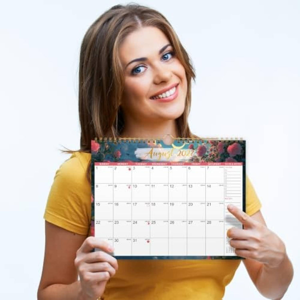 Woman holding a 2027 wall calendar with spiral-bound monthly date grid