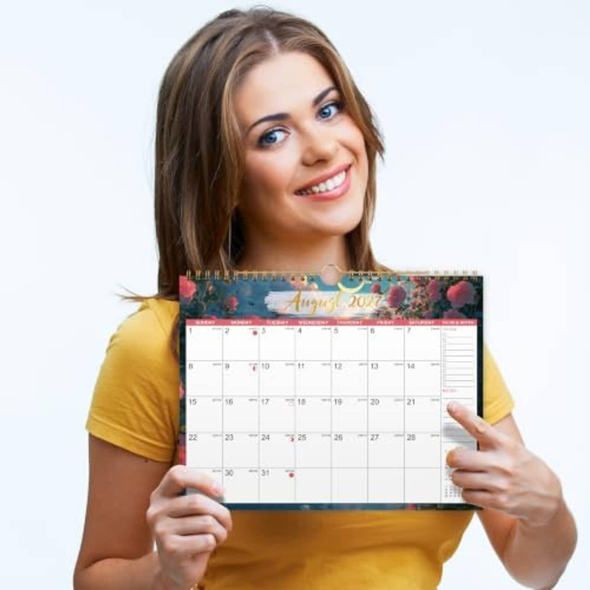 Woman holding a 2027 wall calendar with spiral-bound monthly date grid